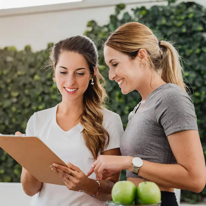 A person consulting with a smiling health coach or nutritionist, looking at a chart or plan